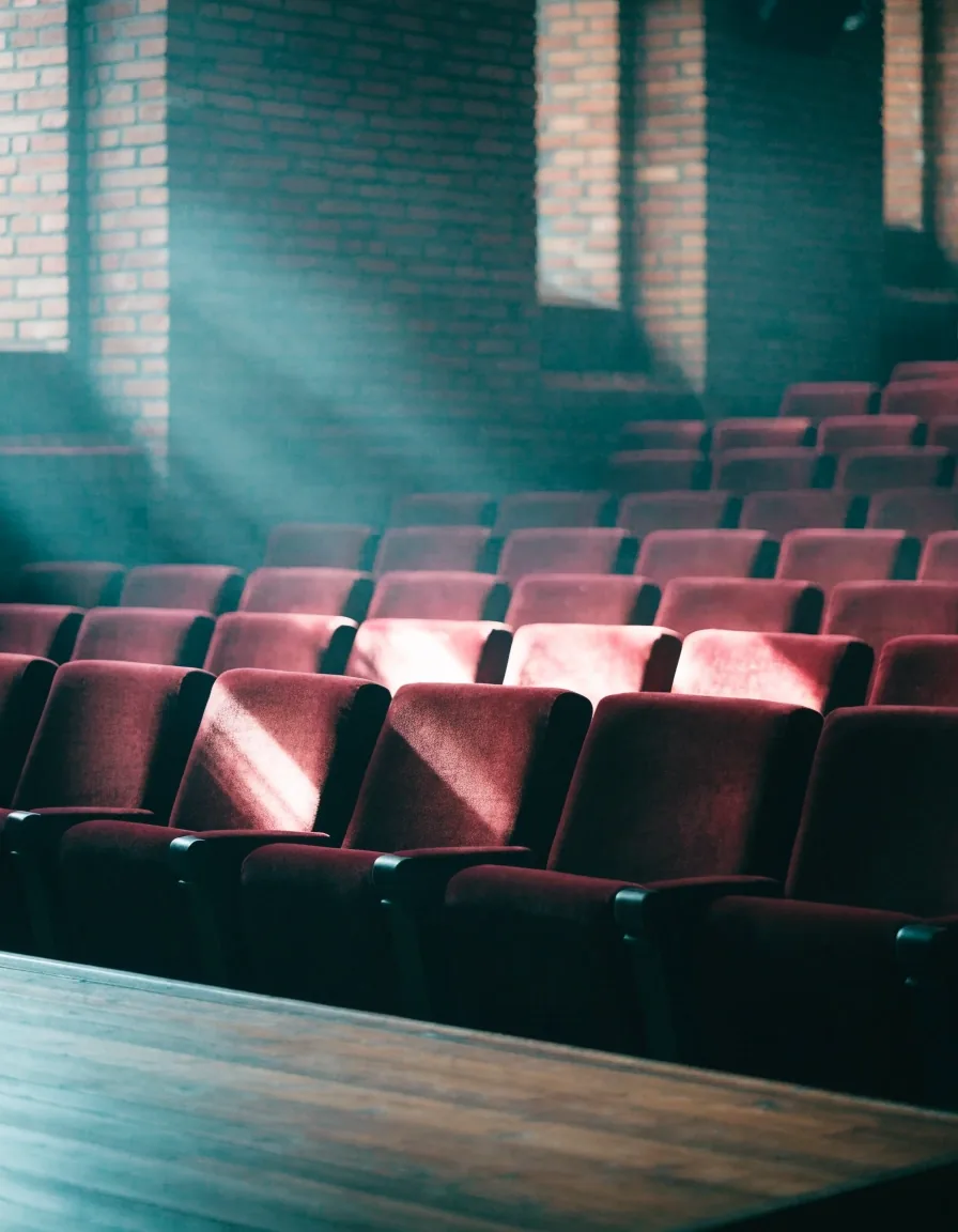 Leeres Theaterfoyer im kühlen Morgenlicht mit roten Sitzen und hölzernem Bühnenboden